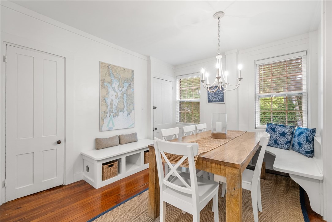 Dining room with a long wooden table, white chairs, and blue-cushioned window seats.