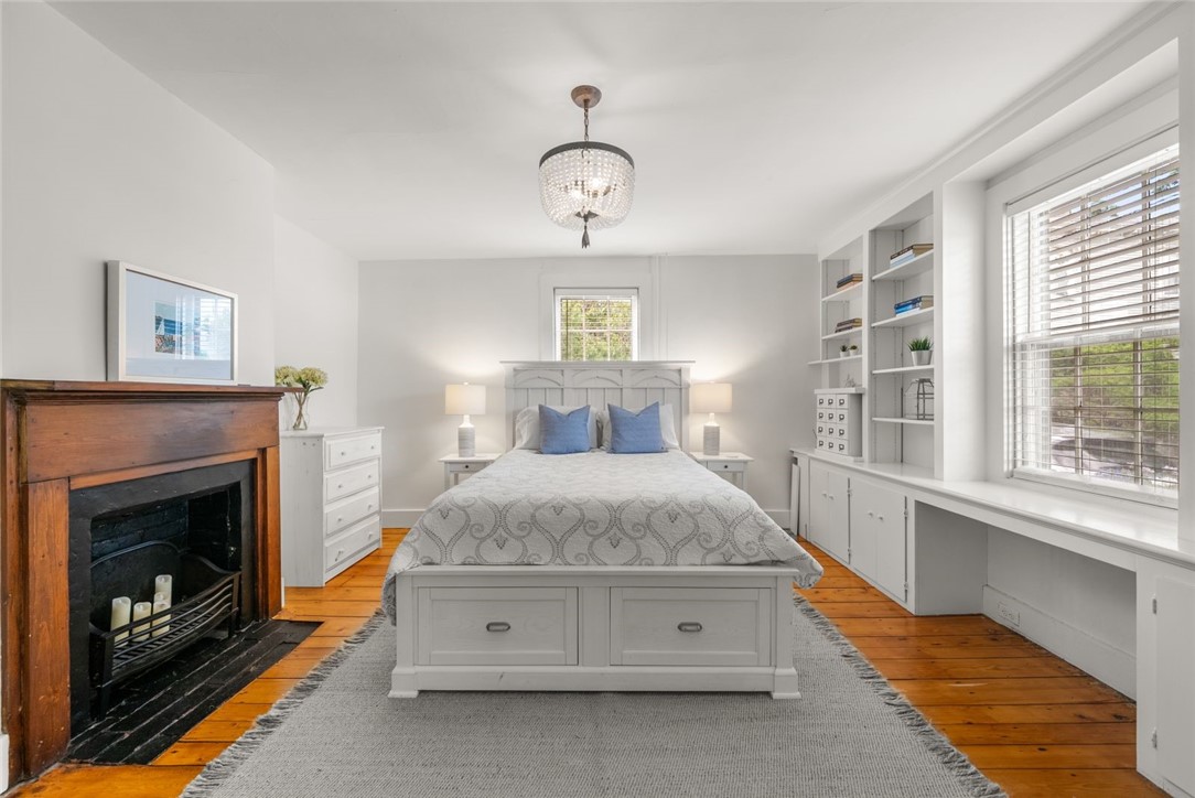 Bedroom with a white bed, wood-burning fireplace, built-in shelves, and hardwood floors.
