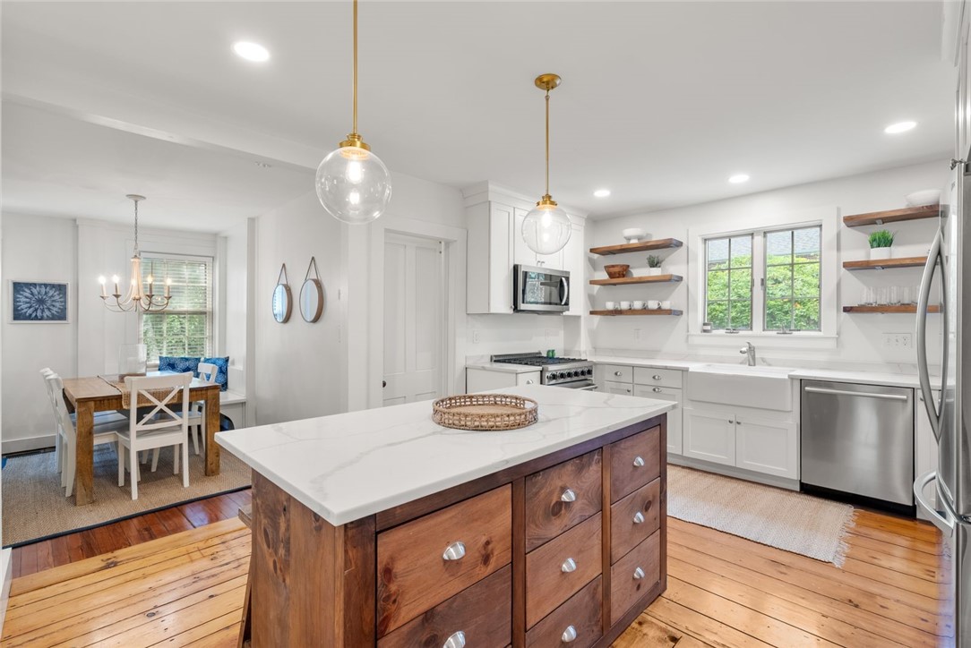 Bright white kitchen with a marble-topped wood island, stainless steel appliances, and adjoining dining area.