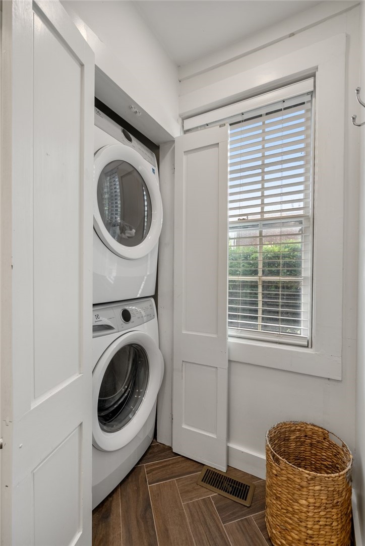 Laundry room with stacked washer and dryer, window blinds, and a woven basket.