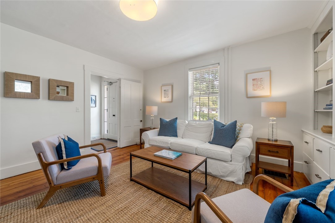 Living room with a white sofa, blue cushions, wood-framed chairs, and hardwood floors.