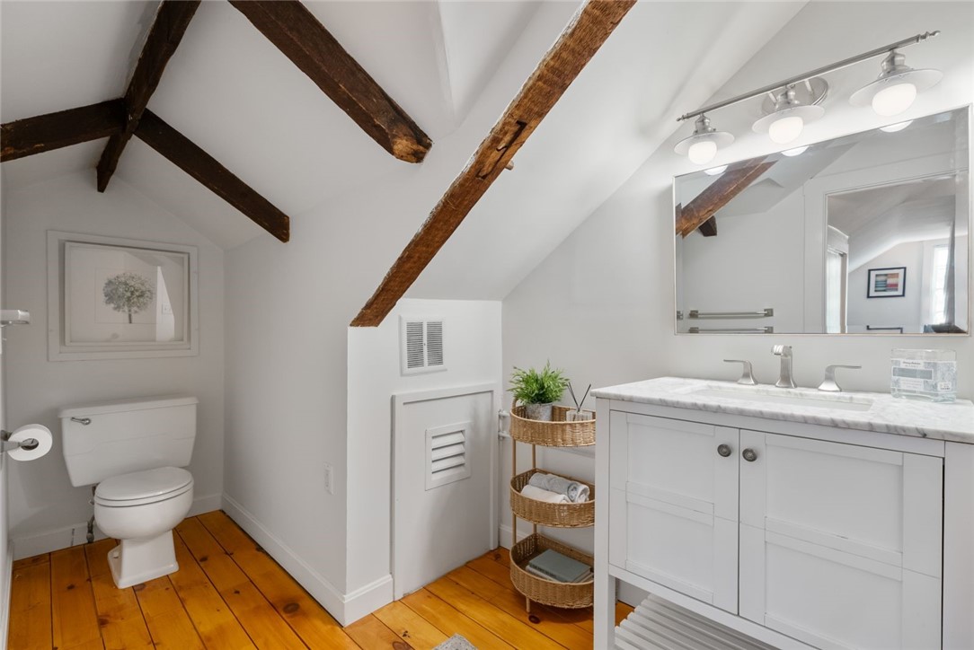 Bathroom with exposed timber beams, a white marble-top vanity, and warm wood flooring.