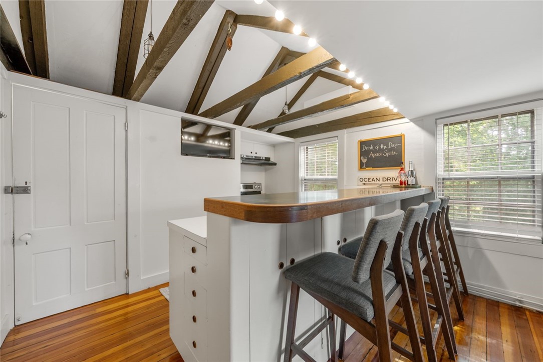 Kitchen with a long wood-trimmed island, gray stools, exposed ceiling beams, and hardwood floors.
