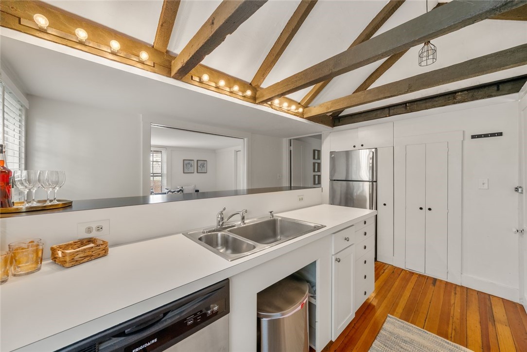 Kitchen with a double-basin sink, stainless appliances, exposed wood ceiling beams, and hardwood floors.