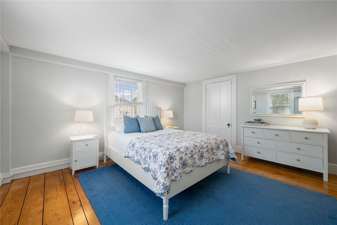 Furnished bedroom with blue floral bedding, a blue rug, and warm wood floors.