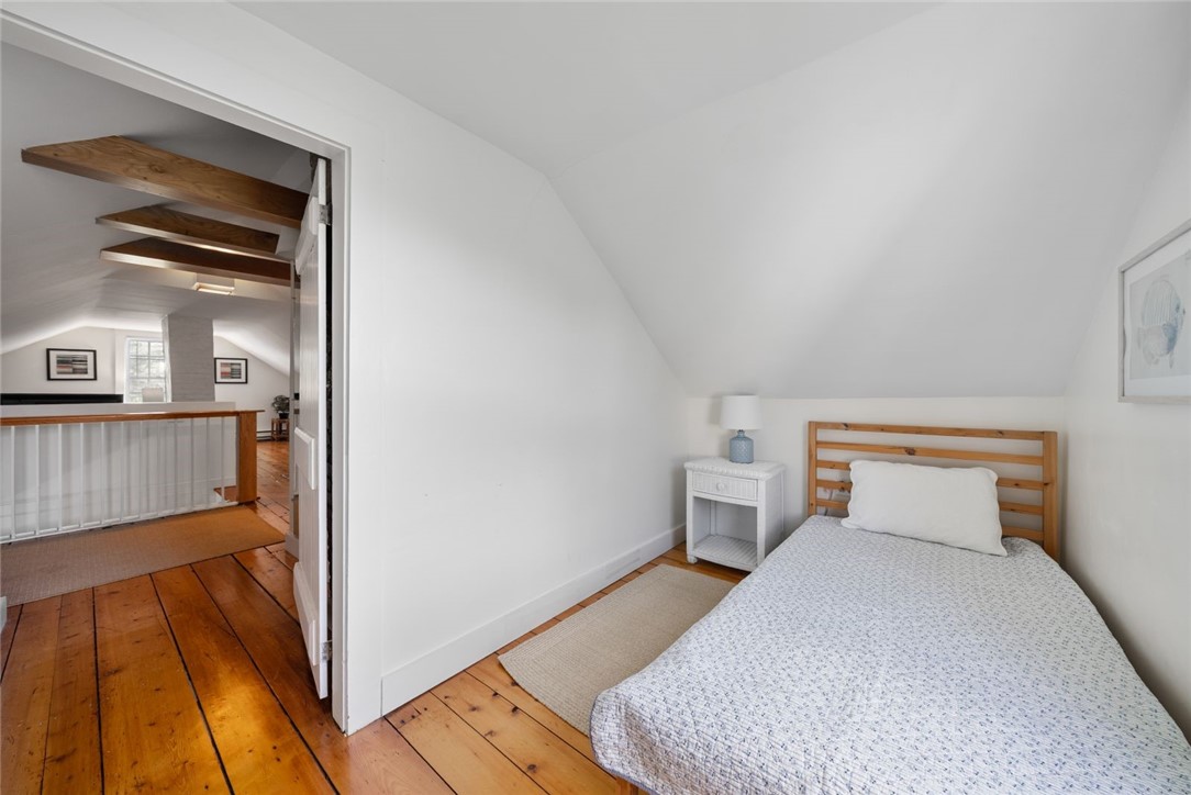Attic bedroom with a wooden bed, sloped ceiling, and plank floors beside an open doorway.