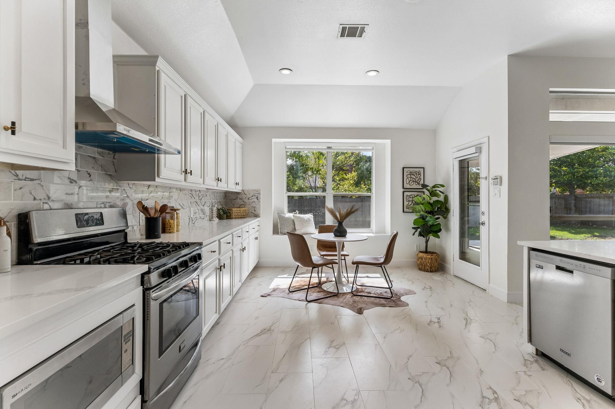 Bright white kitchen with marble-look finishes, stainless gas range, and a small breakfast nook.