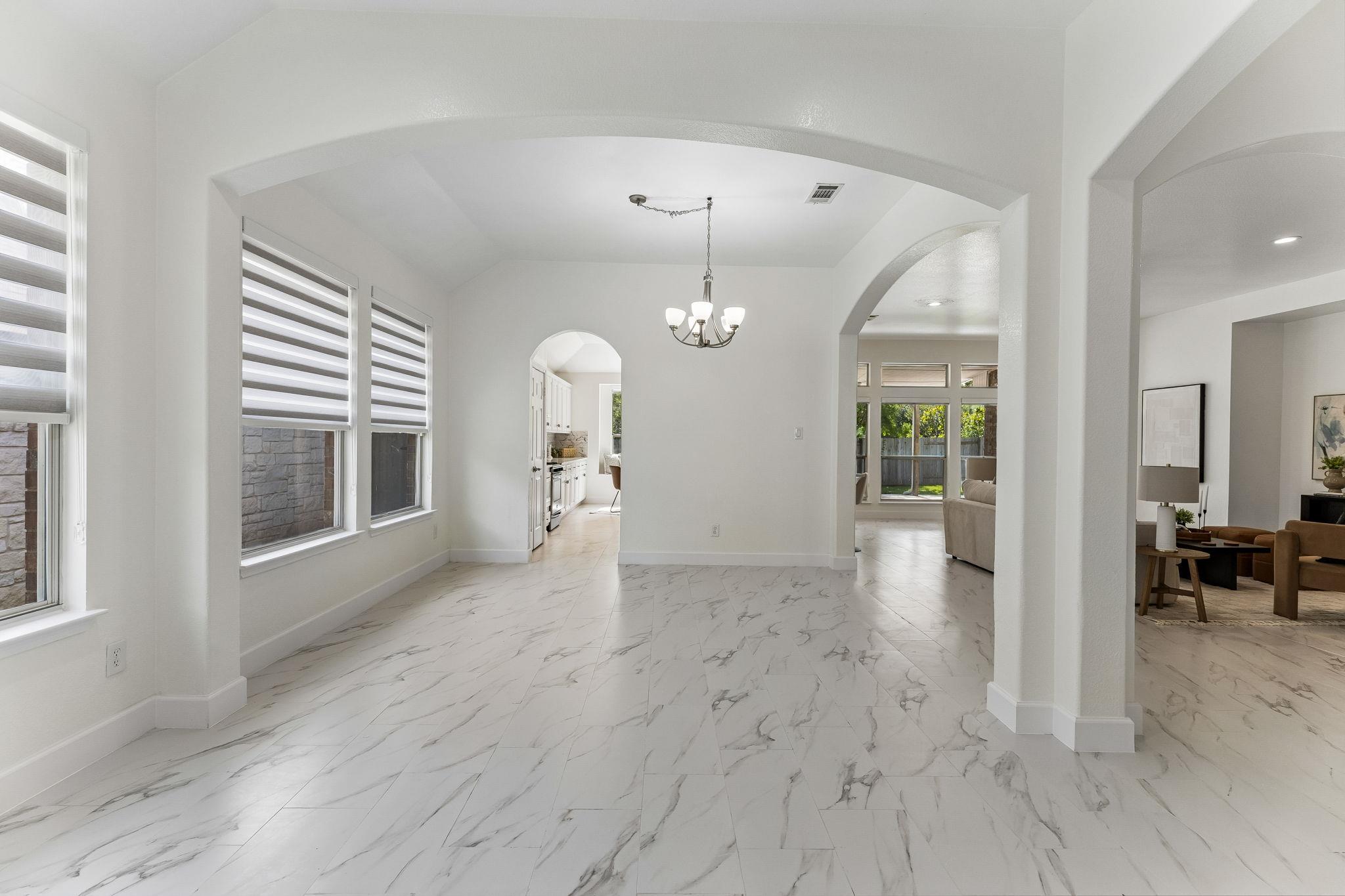 Bright dining area with marble-look tile, striped roller shades, and arched openings to the kitchen and living room.