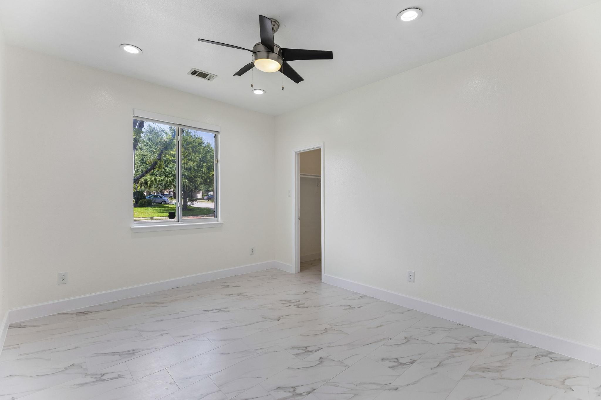 Empty room with marble-look tile flooring, a ceiling fan, and a window overlooking trees.