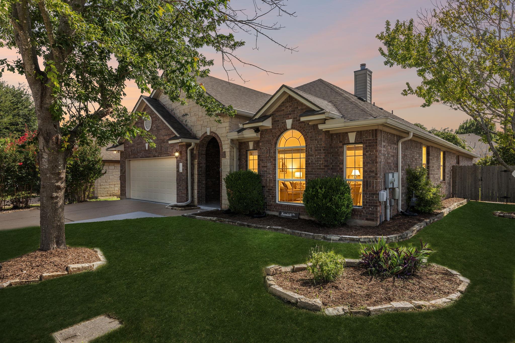 Brick-and-stone home with an attached garage, arched front window, and landscaped lawn at dusk.