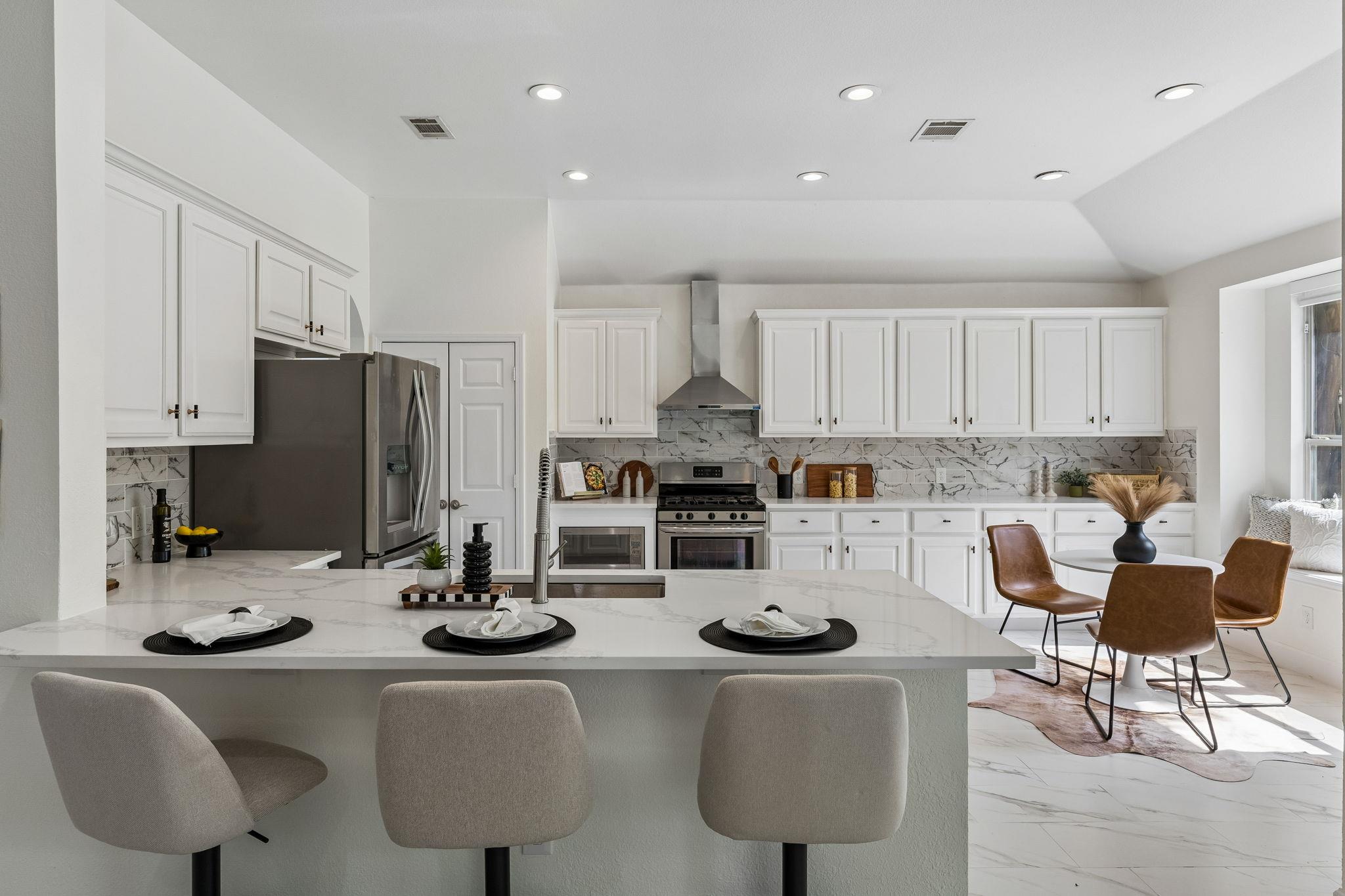 Bright kitchen with a marble island, white cabinetry, stainless appliances, and adjoining dining nook.