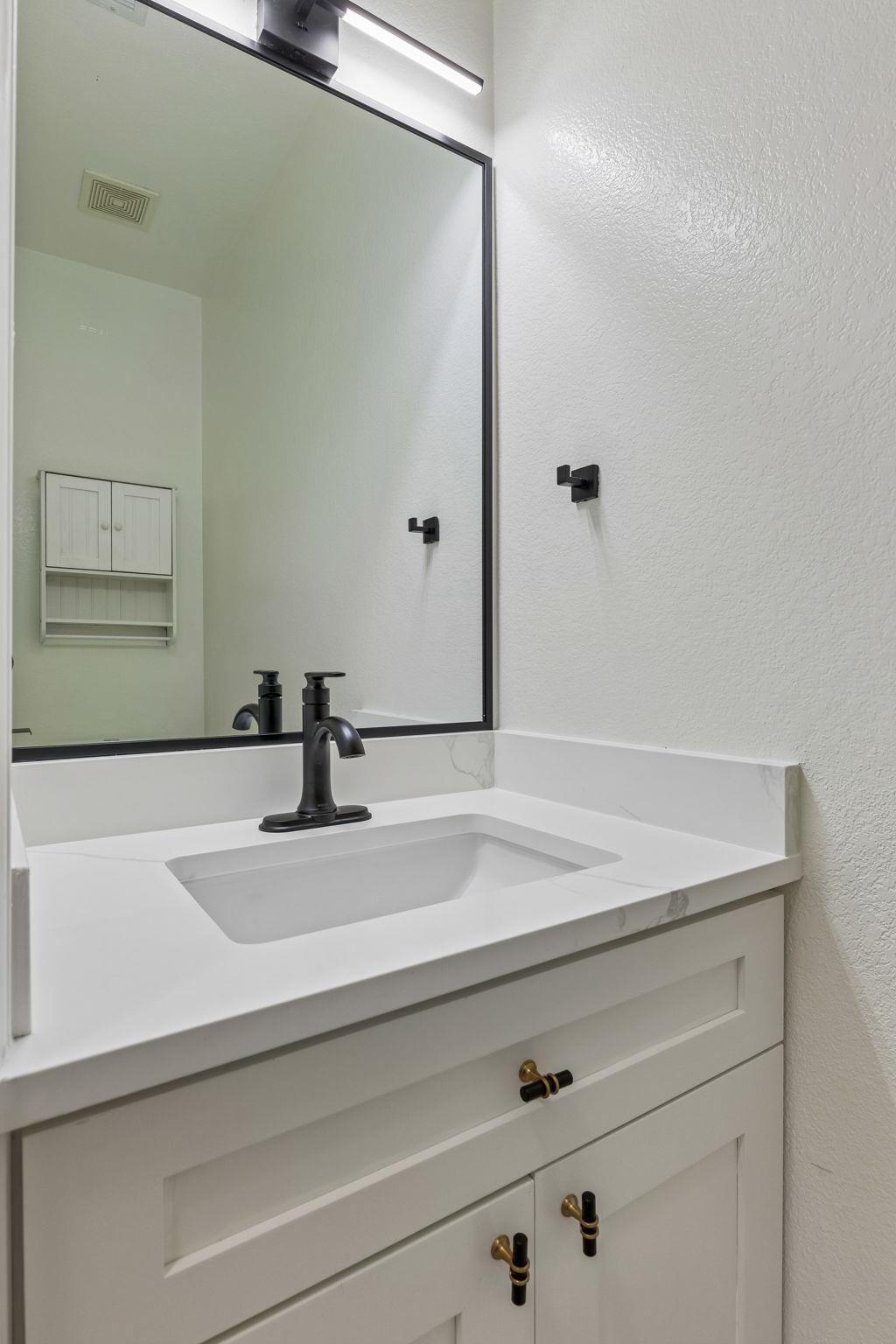Bathroom vanity with a white countertop, undermount sink, black faucet, and large mirror.