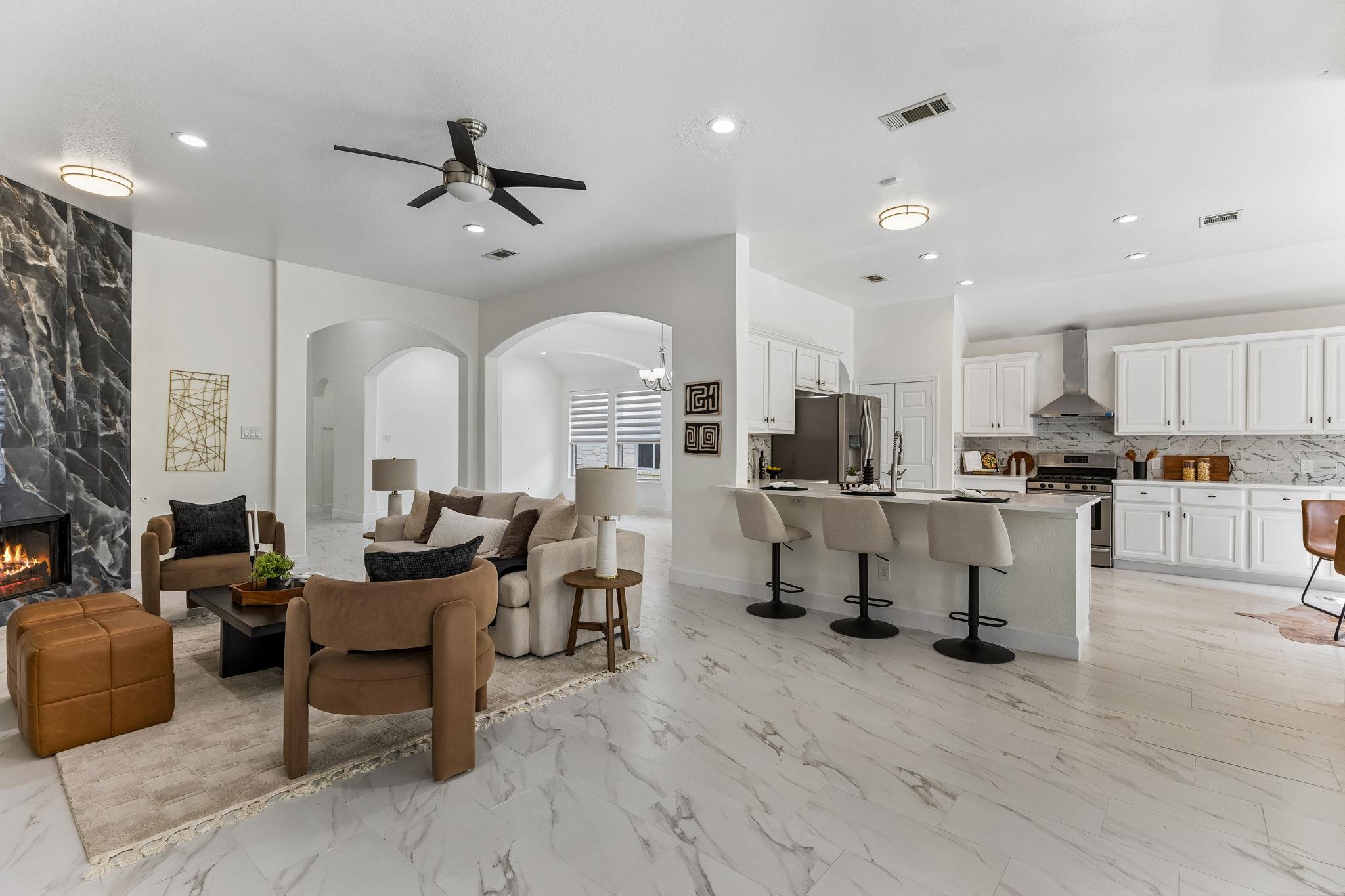Open-plan living room and kitchen with a marble fireplace, island, and neutral furnishings.