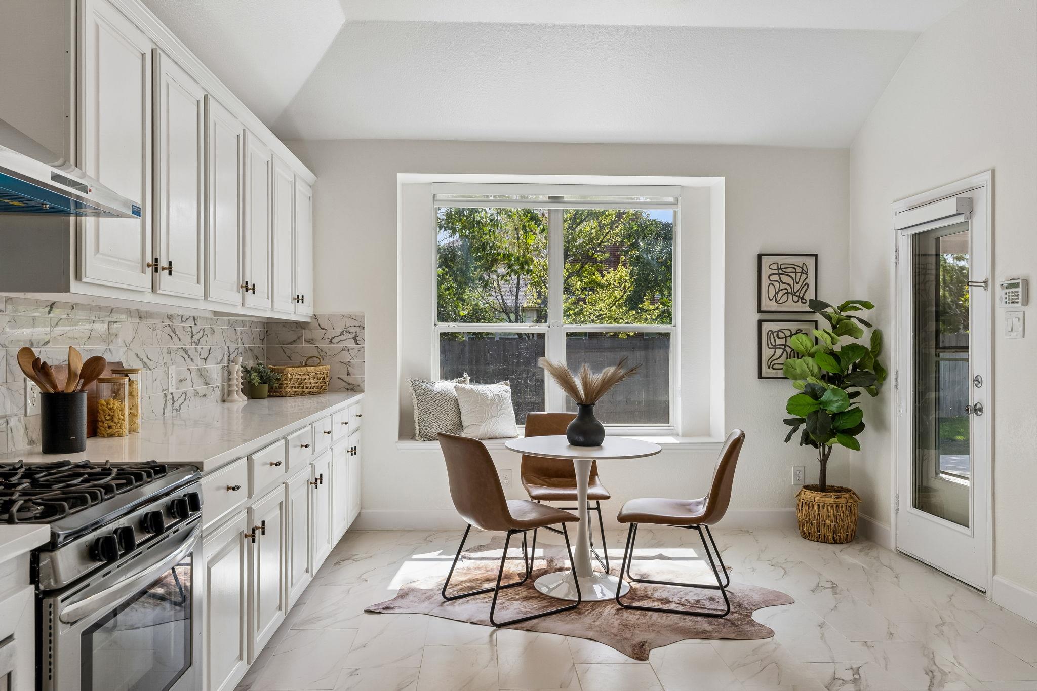 Bright white kitchen with a gas range, marble-look surfaces, and a window-side breakfast nook.