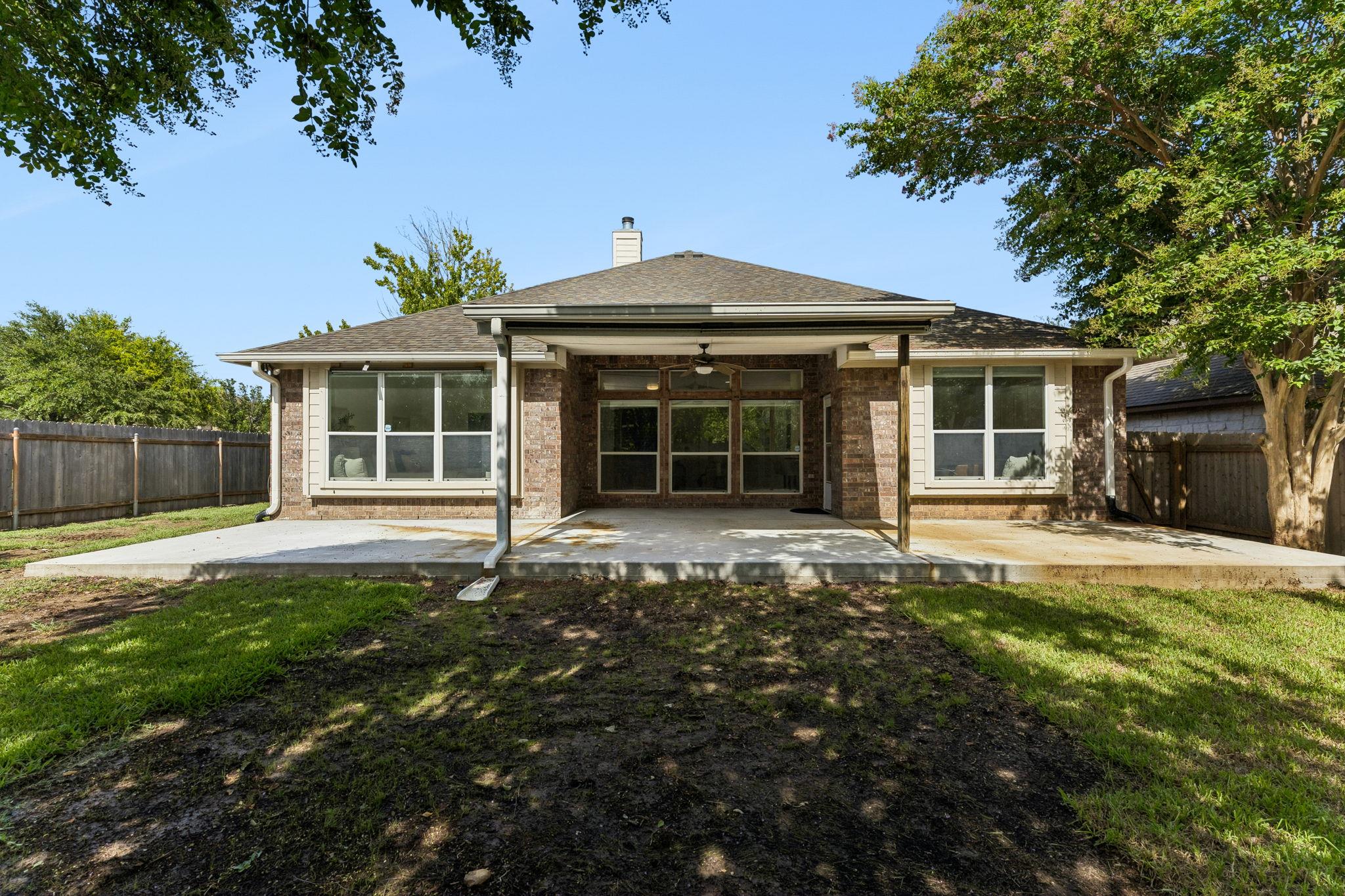 Rear exterior of a brick home with a covered patio and fenced backyard.