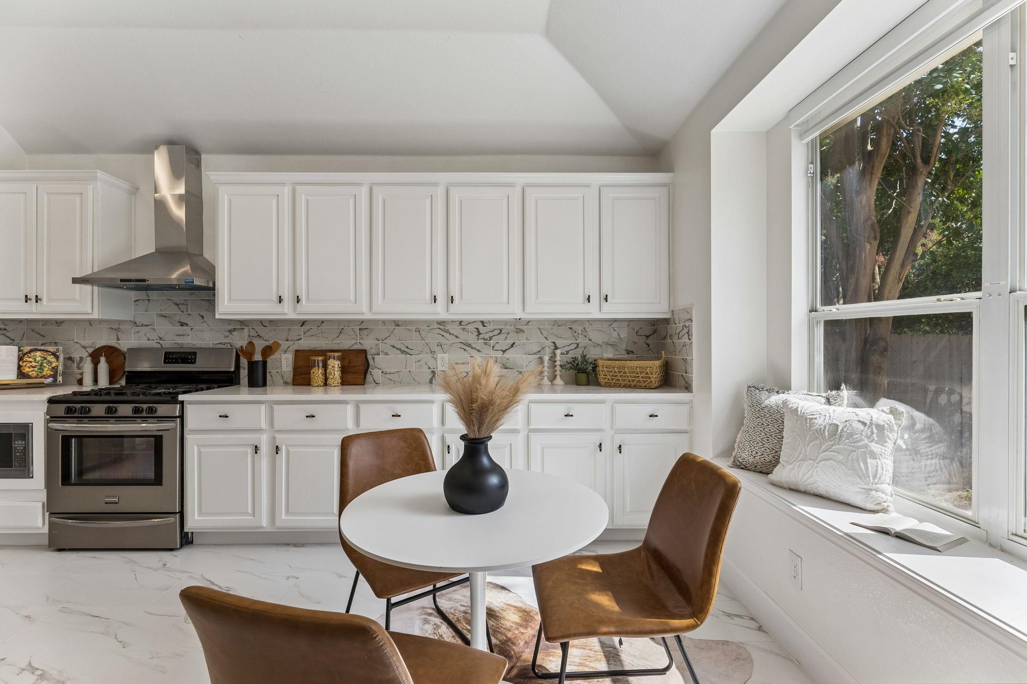 Bright white kitchen with marble-look backsplash, stainless range, and a window-seat dining nook.