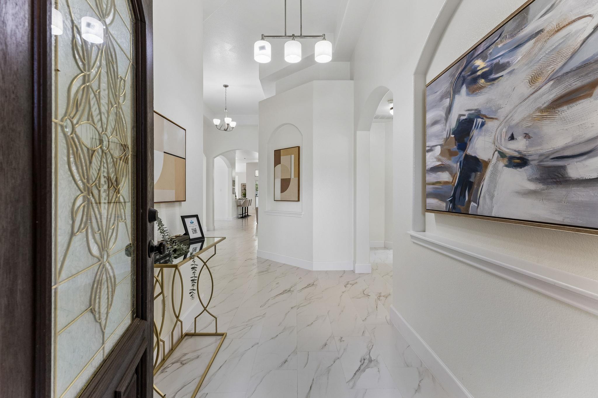 Bright entry foyer with a decorative glass front door, marble-look tile, and a gold console table.