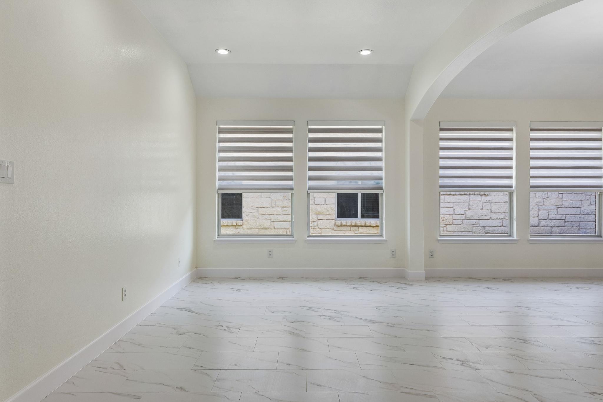 Empty room with marble-look tile floors, four shaded windows, and an arched opening.