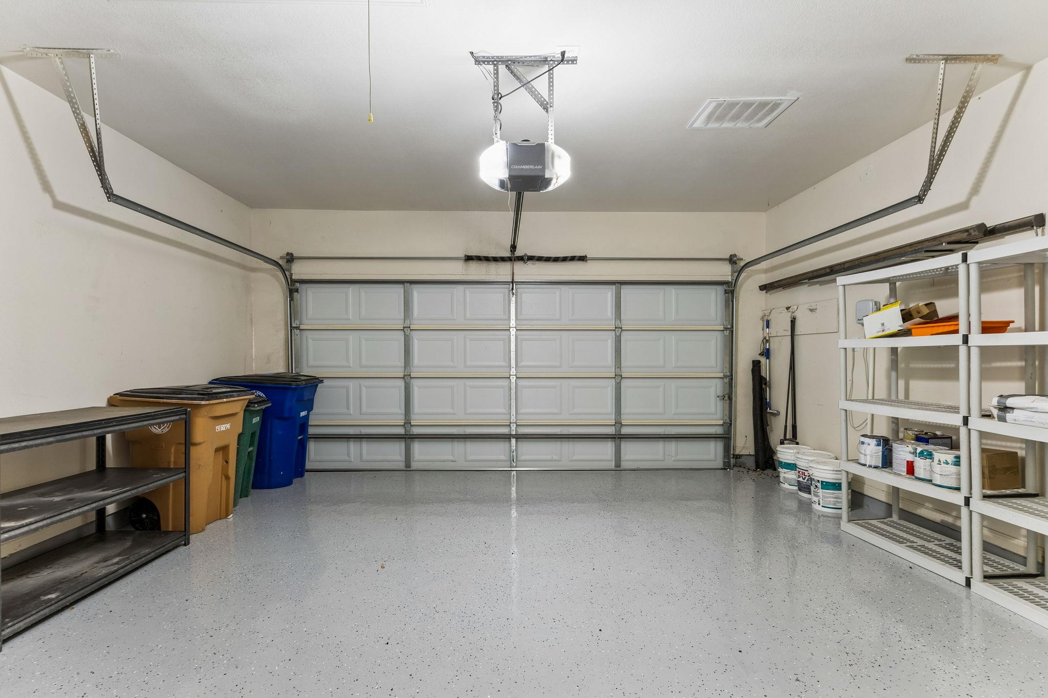 Garage with a speckled floor, closed sectional door, storage shelves, and bins.
