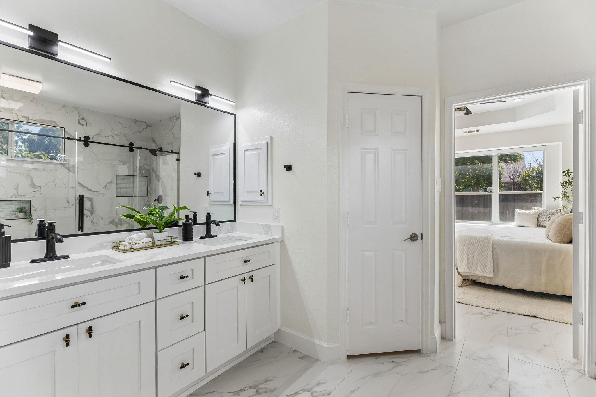 Bathroom with a marble-look double vanity and glass shower, opening to a bedroom.