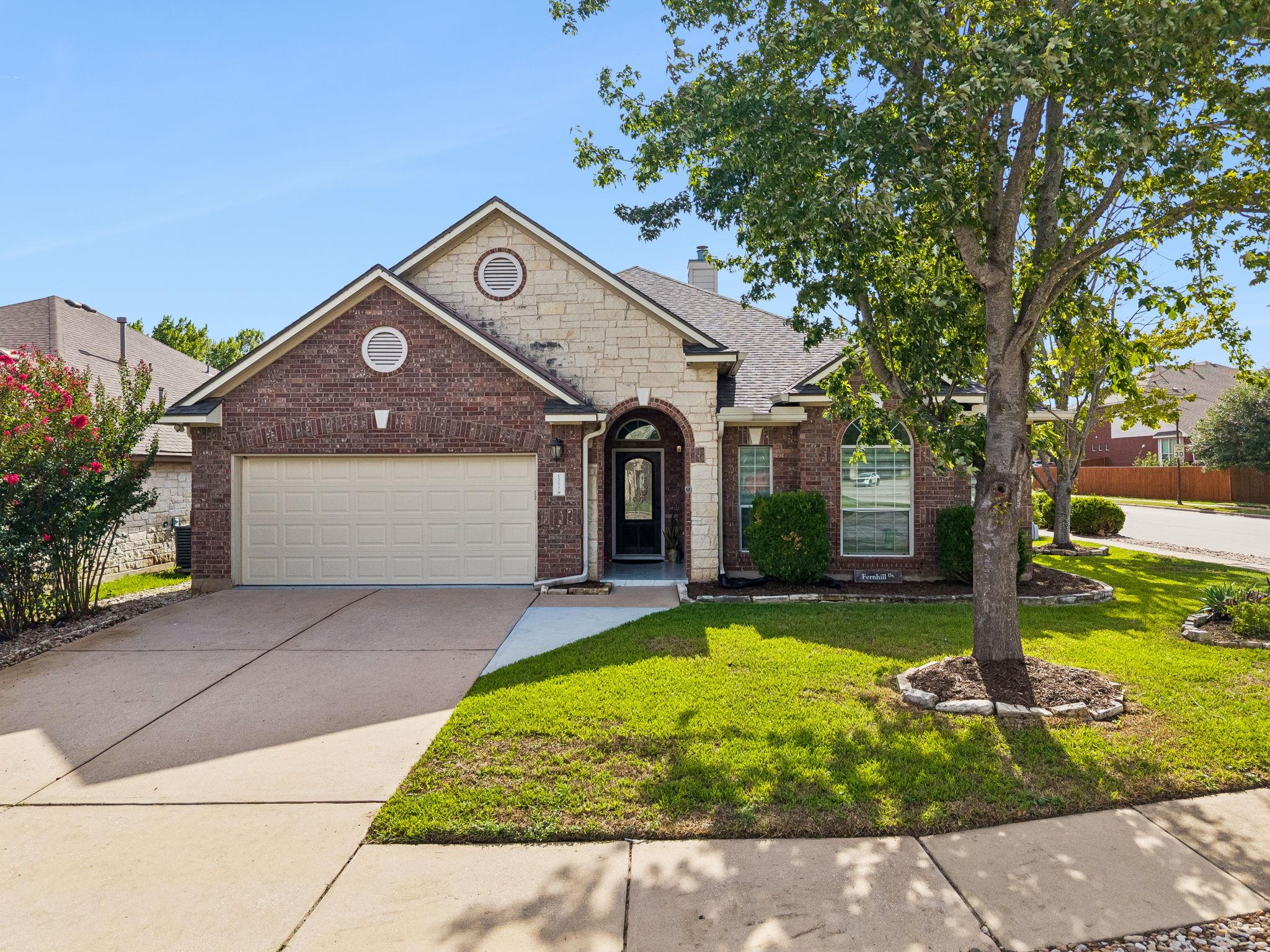 Brick-and-stone home with a two-car garage, arched entry, and large shade tree.