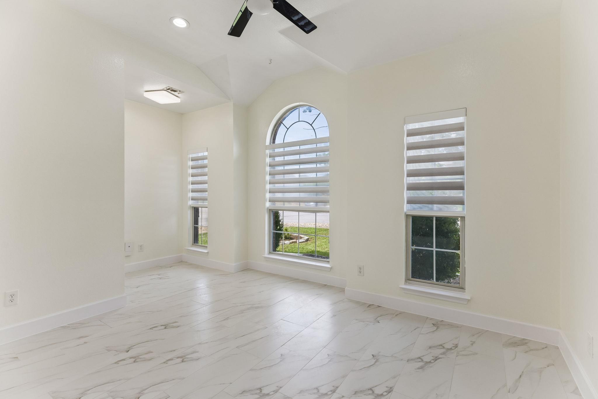 Empty room with a vaulted ceiling, arched window, and marble-look tile flooring.