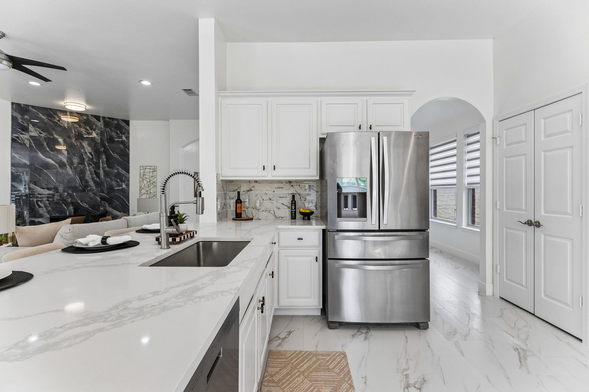 Bright kitchen with white marble counters, stainless steel appliances, and an island sink.