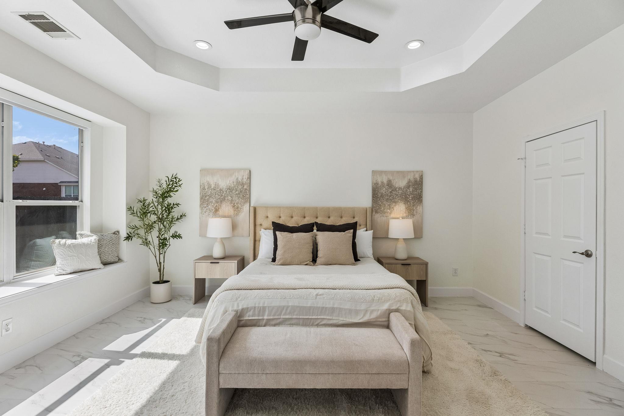 Staged bedroom with a tufted bed, marble-look tile floor, and bright window.