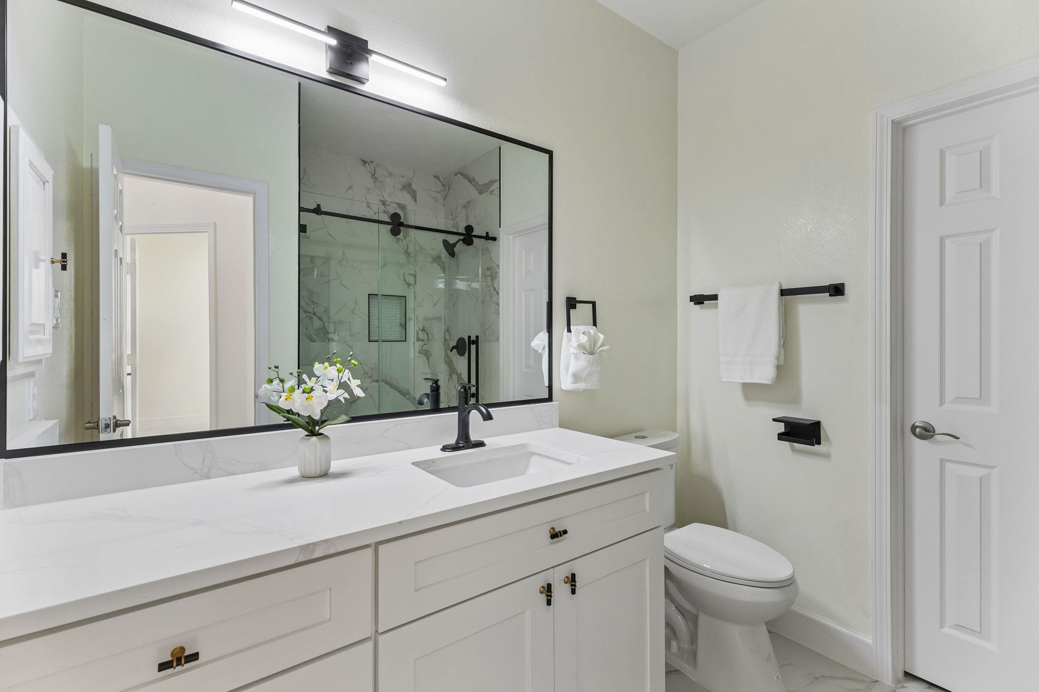 Bathroom with a white double vanity, marble-look shower, and black fixtures.