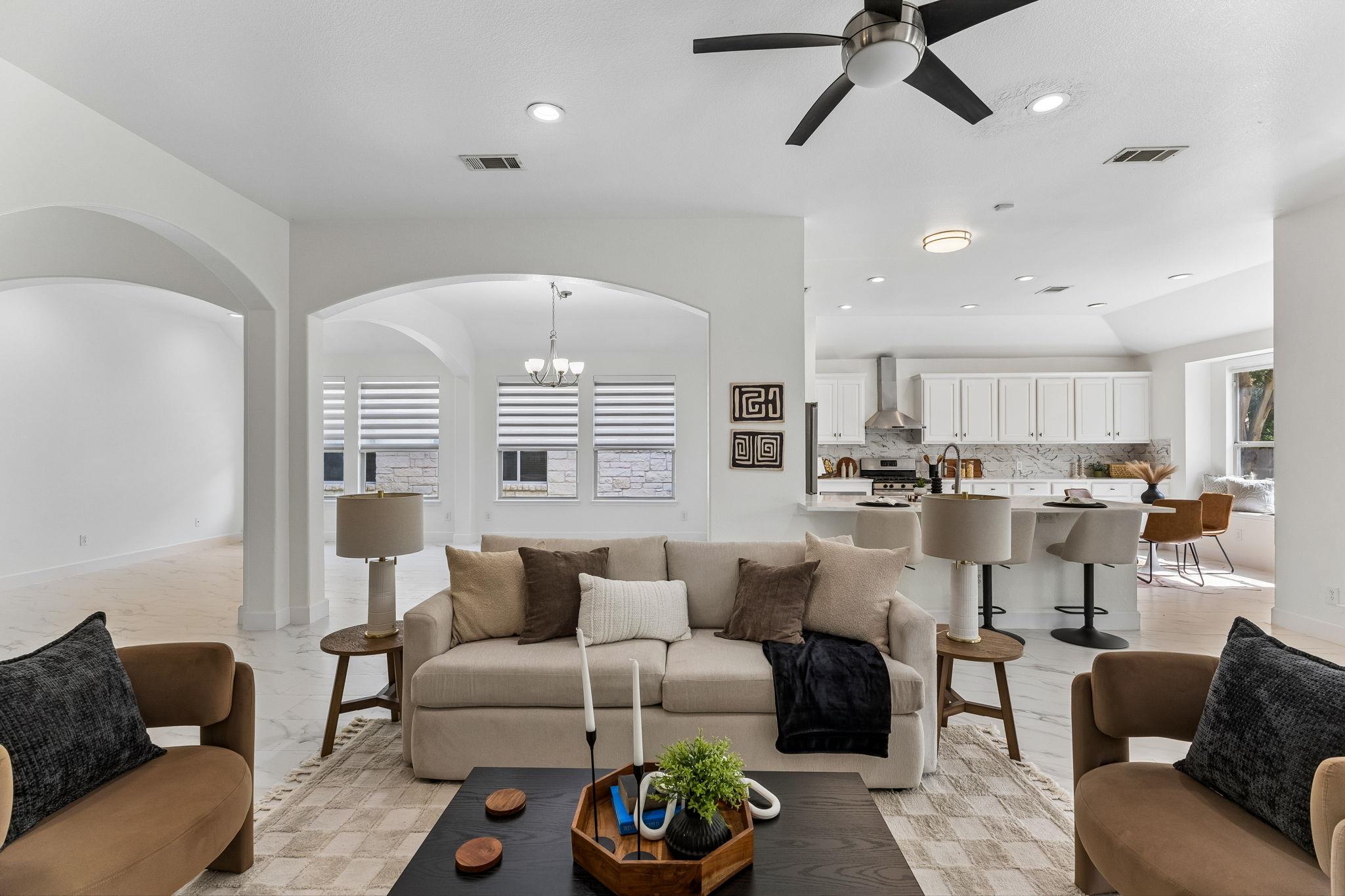 Staged open-plan living room and kitchen with arched openings, white cabinetry, and a central island.