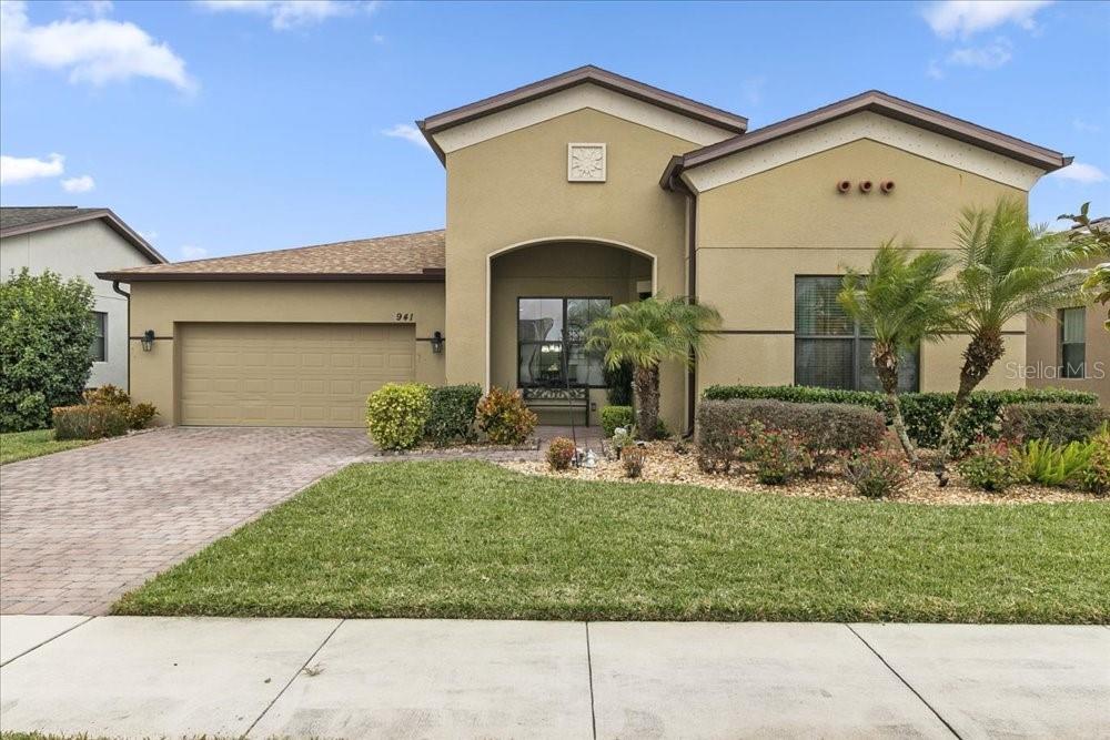 Stucco home with a two-car garage, arched entry, paver driveway, and landscaped front lawn.