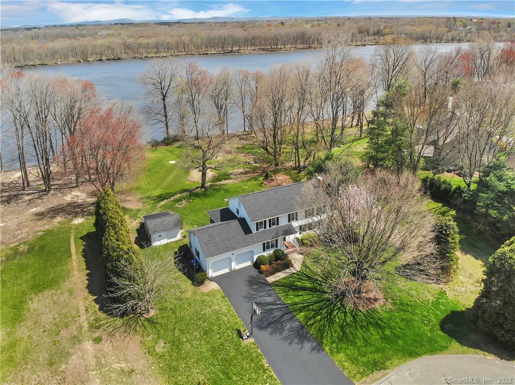 Aerial view of a house beside a broad river, with green lawns and mature trees.