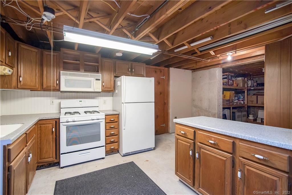 Basement kitchen with wood cabinets, white appliances, and exposed ceiling joists.