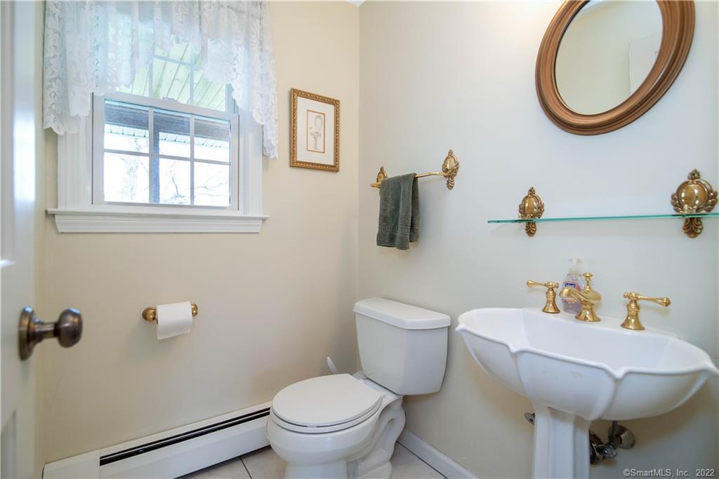 Bathroom with a white pedestal sink, toilet, brass fixtures, and lace curtains.