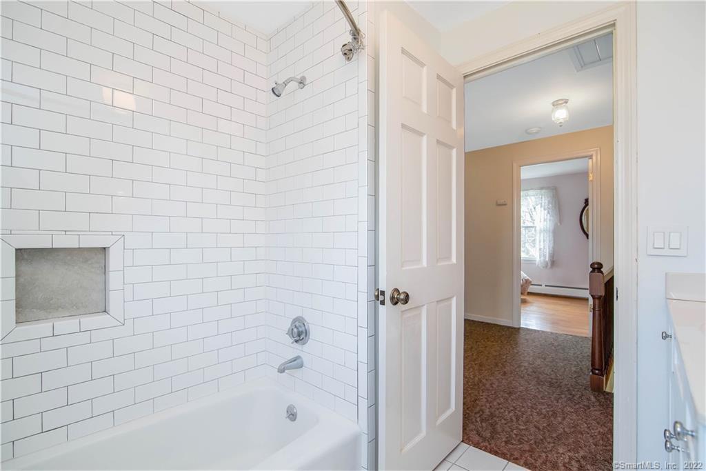 Bathroom with a white subway-tile tub and shower, recessed niche, and open doorway to the hall.
