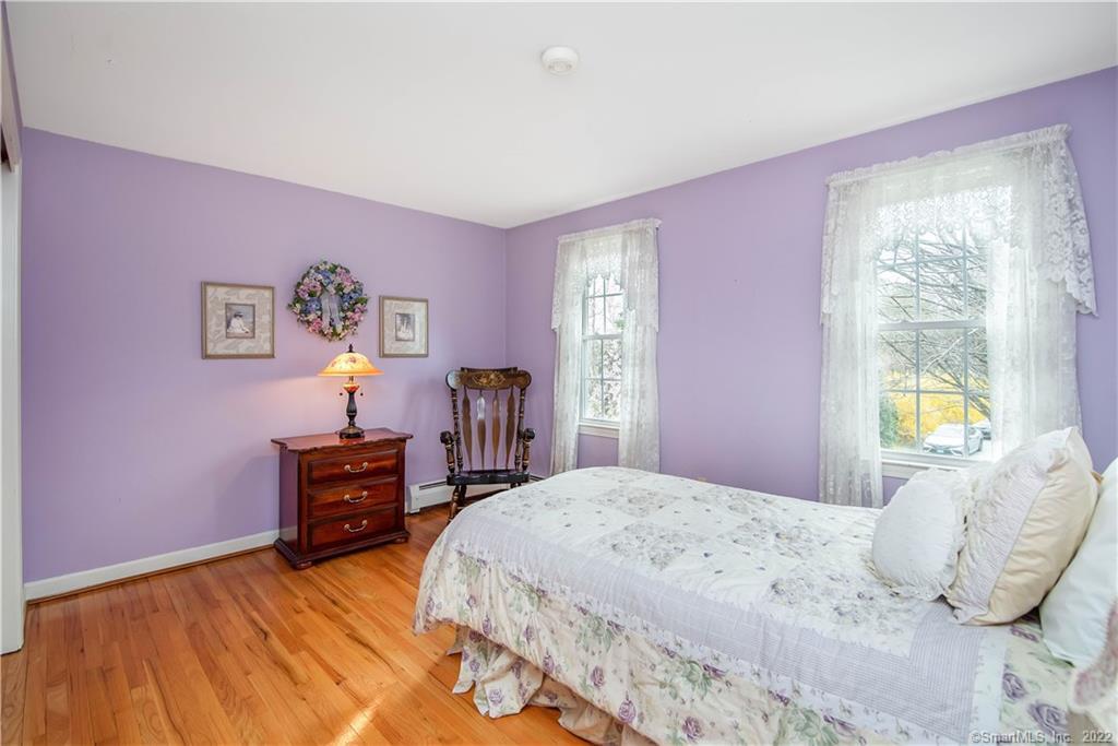 Bedroom with lavender walls, hardwood floors, a floral bedspread, and lace-curtained windows.