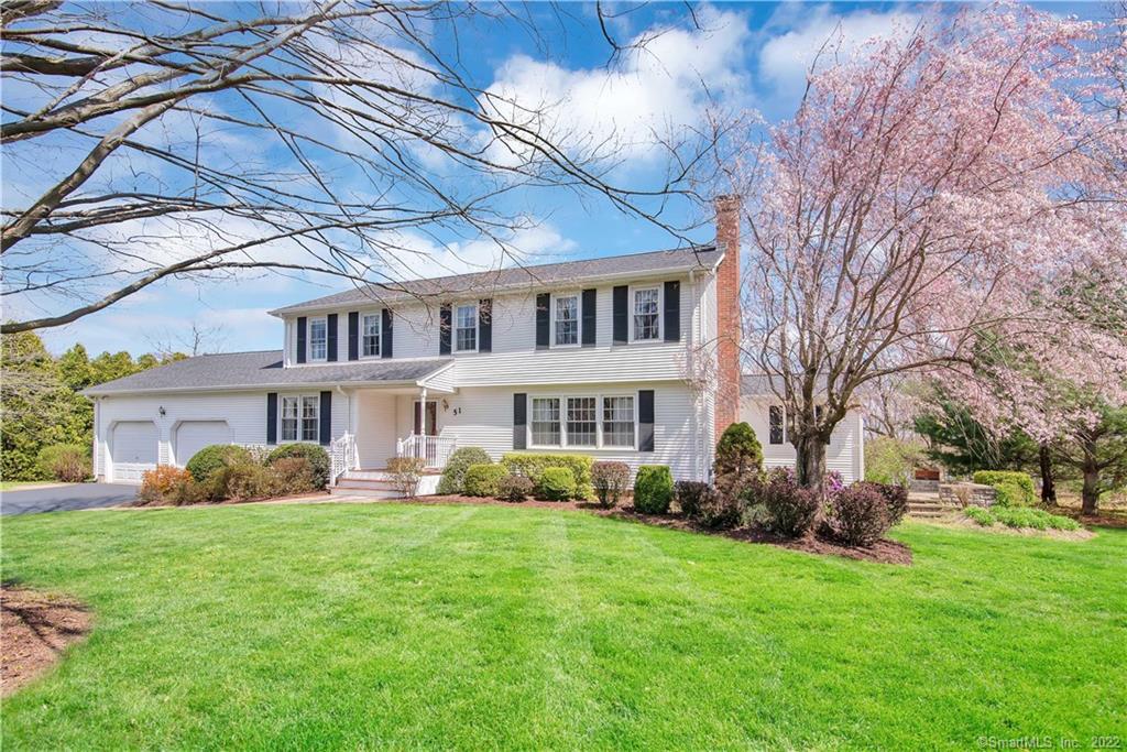 White two-story house with black shutters, an attached garage, and a pink-blossoming tree beside the lawn.