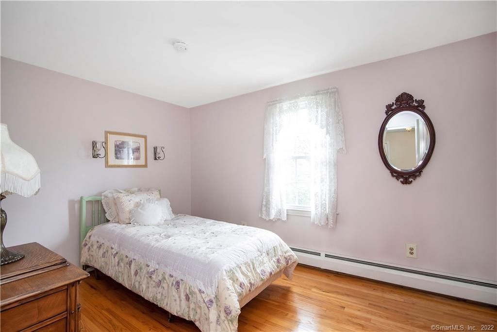 Bedroom with a floral bed, green headboard, hardwood floors, and an ornate oval mirror.