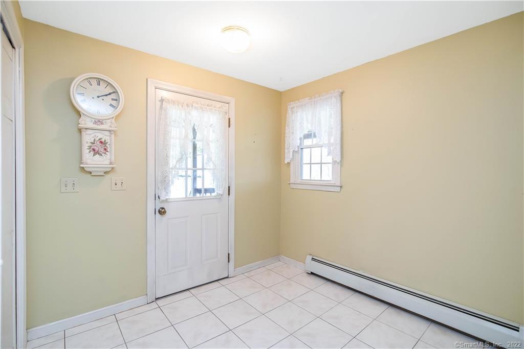 Empty entry room with white tile flooring, a lace-covered exterior door window, and a wall clock.