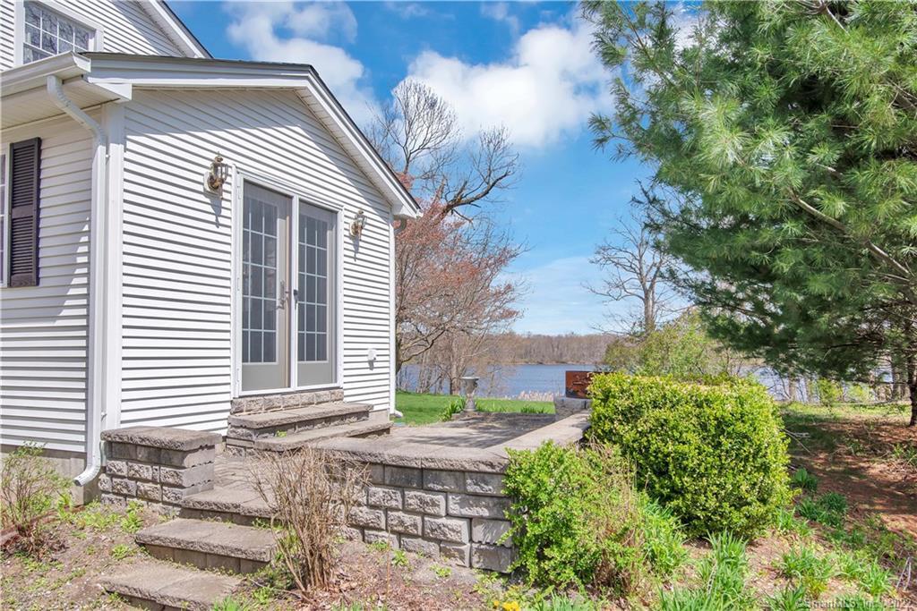 White-sided house with stone patio and steps overlooking a lake.