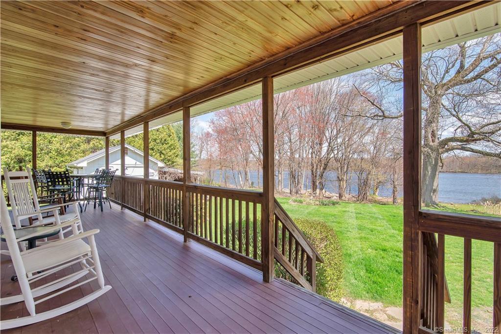 Covered porch with rocking chairs overlooking a lawn and water through leafless trees.