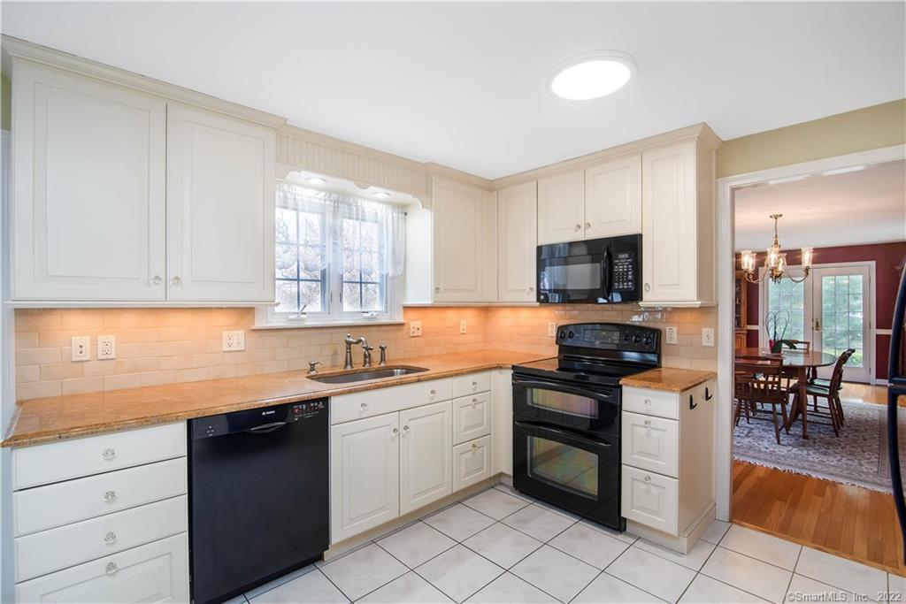Kitchen with white cabinets, black appliances, and a window above the sink; dining room visible through doorway.