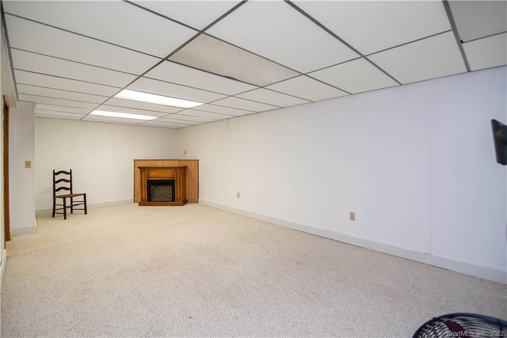 Carpeted room with a wood-trimmed fireplace and suspended tile ceiling.