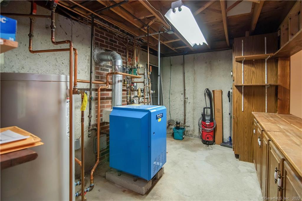 Basement mechanical room with a blue boiler, exposed pipes, a large tank, and built-in wooden storage.