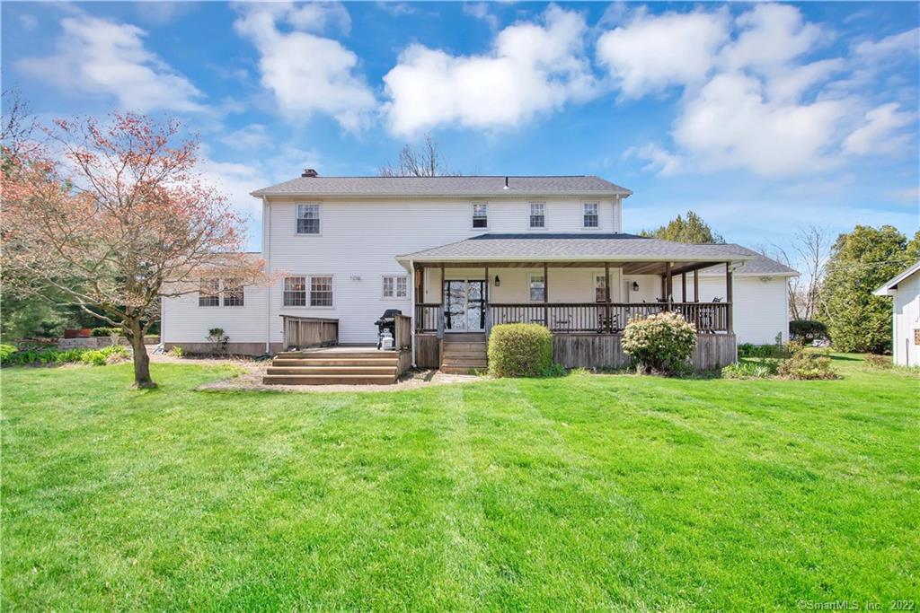 Two-story white home with a covered wooden deck overlooking a broad green lawn.