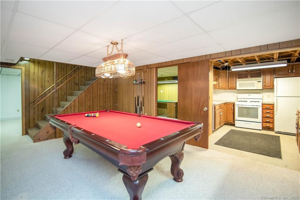 Basement game room with a red pool table, wood-paneled walls, and adjoining kitchenette.