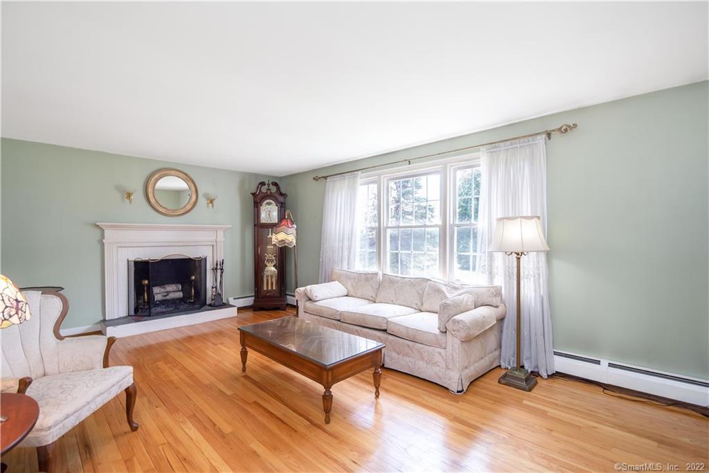 Living room with a white fireplace, cream sofa, hardwood floors, and large curtained windows.