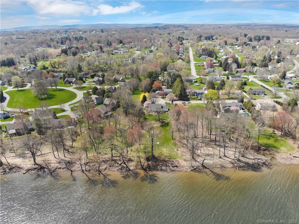 Aerial view of a riverside neighborhood with a circular park and wooded hills.