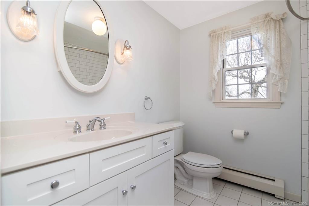 Bathroom with a long white vanity, oval mirror, and lace-curtained window.