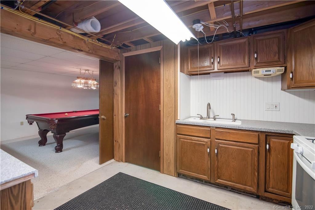 Basement kitchenette with wood cabinets and sink, opening to a room with a pool table.